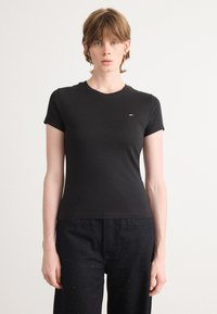 T-shirt noir à manches courtes en tissu doux, avec un col rond et un petit logo sur la poitrine gauche. Associé à un pantalon sombre à motifs.