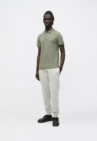 Zielona koszulka polo z kołnierzykiem i trzema guzikami, zestawiona z jasnoszarymi dresami z troczkiem i logo. Czarnie tenisówki dopełniają wygląd.