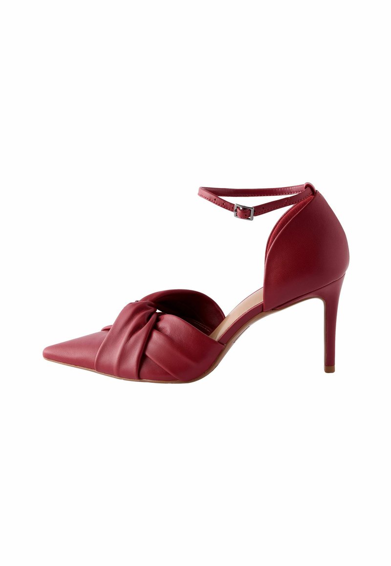 Chaussure à talon haut en cuir rouge avec un bout pointu, un design à l'avant noué et une bride à la cheville. Texture lisse et silhouette élégante.