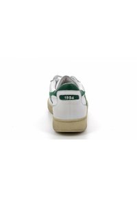 Sneaker bianca con accenti verdi, suola in gomma testurizzata e linguetta posteriore con la scritta "1984". Presenta lacci e una tomaia liscia simile alla pelle.