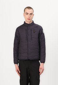 Veste rembourrée noire avec motif en vagues, boutons-pression, deux poches avant et col montant, assortie avec un pantalon cargo noir.