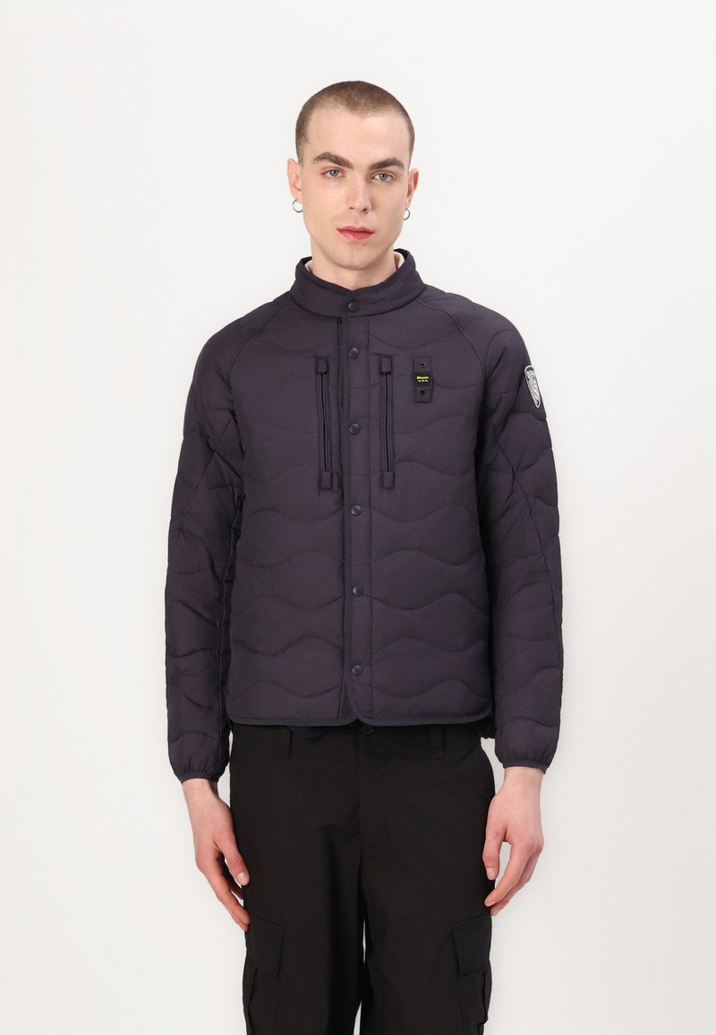 Veste rembourrée noire avec motif en vagues, boutons-pression, deux poches avant et col montant, assortie avec un pantalon cargo noir.