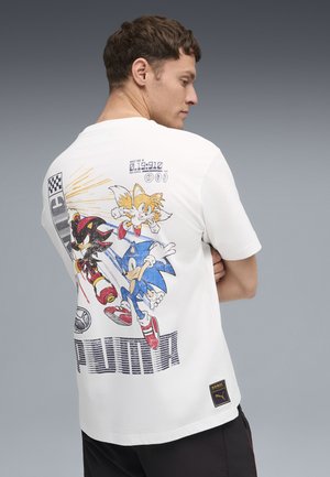 Hombre con camiseta blanca de Puma con gráfico de carreras de los personajes Sonic the Hedgehog, Tails y Shadow en la espalda.