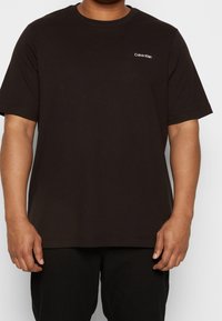 Svart bomull t-shirt med korta ärmar, rund halsringning och en liten vit "Calvin Klein" logotyp på vänster bröst. Slät textur, avslappnad passform.