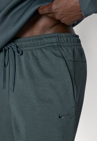 Donkergroene sweatpants met elastische tailleband en koord. Zacht materiaal, zijzakken, met een klein zwart Nike-logo.