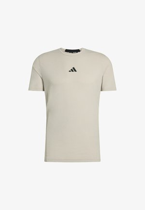 Camiseta de algodón de manga corta en color beige claro, con un logo negro de Adidas en el pecho. Cuello redondo y corte estándar.