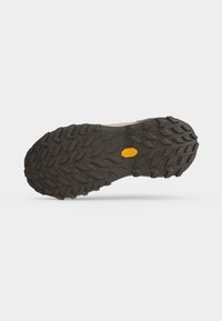 Sole of a hiking shoe with deep treads for grip and a yellow Vibram logo in the center on a plain light background.