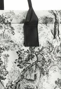Schwarz-weiße Tragetasche mit einer strukturierten, gemusterten Oberfläche, die Bäume und Laub zeigt. Schwarze Träger sind an den Oberkanten befestigt.