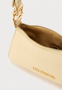 Μπεζ δερμάτινη τσάντα χειρός με χρυσά μεταλλικά στοιχεία, φερμουάρ και ανάγλυφο λογότυπο "LOVE MOSCHINO" στο μπροστινό μέρος. Το εσωτερικό έχει λεία υφή.