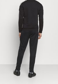 Completo sportivo nero con strisce laterali bianche, composto da un sudore con collo rotondo e pantaloni affusolati, realizzato in tessuto liscio e traspirante.