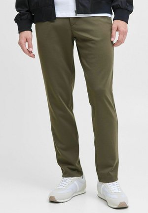 Pantalones ajustados verde oliva hechos de tela elástica, con una textura suave, combinados con una camiseta blanca sencilla y zapatillas blancas.