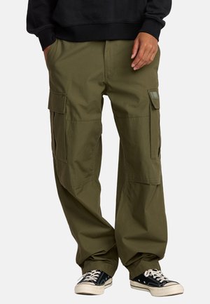Olijfgroene cargobroek met meerdere zijzakken, een relaxte pasvorm en duurzame stof. Gepaard met zwarte sneakers met witte accenten.