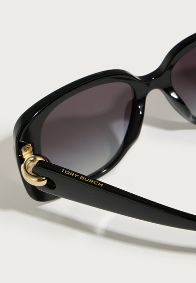 Črne sončne očala z velikim, zaobljenim okvirjem, temno gradientnimi lečami in zlatim okroglim detajlom na ročaju, ki nosi vgravirano "Tory Burch."