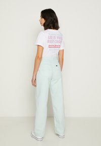 Camiseta branca de mangas curtas com texto gráfico nas costas. Calças largas de alta cintura em verde menta claro. Ténis brancos com detalhes em preto.