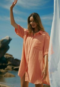 Pfirsichfarbiges, übergroßes, knöpfbares Hemd aus leichtem, strukturiertem Stoff mit einer einzelnen Brusttasche und kurzen Ärmeln.