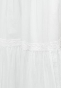 Λευκό ύφασμα με διάφανη, ρυτιδωτή υφή και οριζόντια λεπτομέρεια δαντέλας.