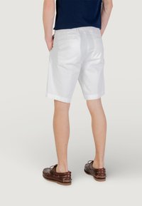Shorts blancs à coupe droite, poches arrières visibles et texture lisse. Associés à des chaussures marron avec des détails à lacets.