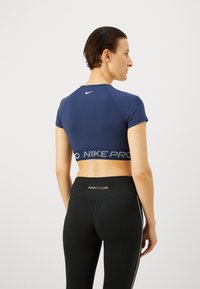 Top atlético recortado de color azul marino con mangas cortas, presenta una banda elástica acanalada con el texto "NIKE PRO". Combinado con leggings negros de cintura alta.