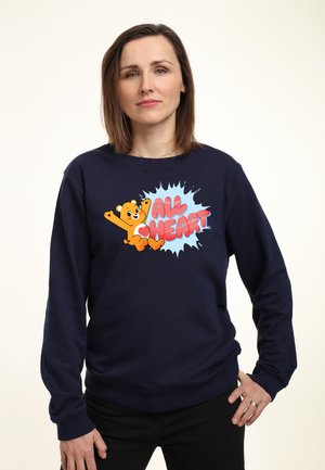 Sweatshirt marine avec un ours en dessin animé coloré et le texte "ALL HEART" à l'intérieur d'une éclaboussure bleu clair, fabriqué dans un tissu doux et avec une coupe décontractée.