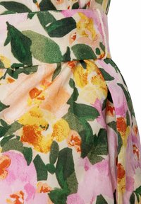 Blumiger Rock mit einem hellrosa Hintergrund, verziert mit gelben, orangenen und grünen Blumen, akzentuiert durch einen Stoffgürtel und ein plissiertes Design.