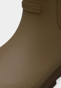 Καφέ ελαστική μπότα με λεία επιφάνεια, που διαθέτει λογότυπο Tretorn στον επάνω ιμάντα και υφή στη σόλα για καλύτερη πρόσφυση.