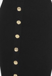 Jupe en tissu côtelé noir avec une rangée verticale de six boutons décoratifs dorés brillants au centre avant.