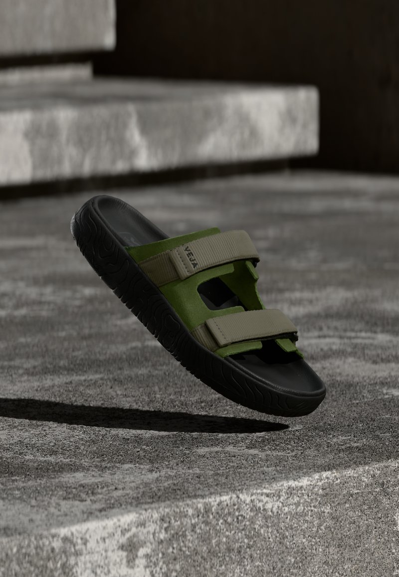 Sandale à glissière verte et noire avec deux brides ajustables, fabriquée en matériau souple. Semelle en caoutchouc texturée, avec un design découpé.
