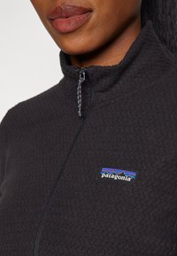 Black fleece pullover with a high collar, featuring a quarter zip and a multicolored Patagonia logo on the chest. Textured fabric.