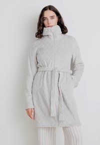 Roa gri deschis, matlasat, cu guler înalt, talie căptușită, mâneci lungi și fermoar în faț�ă. Textură moale cu modele în diamant.