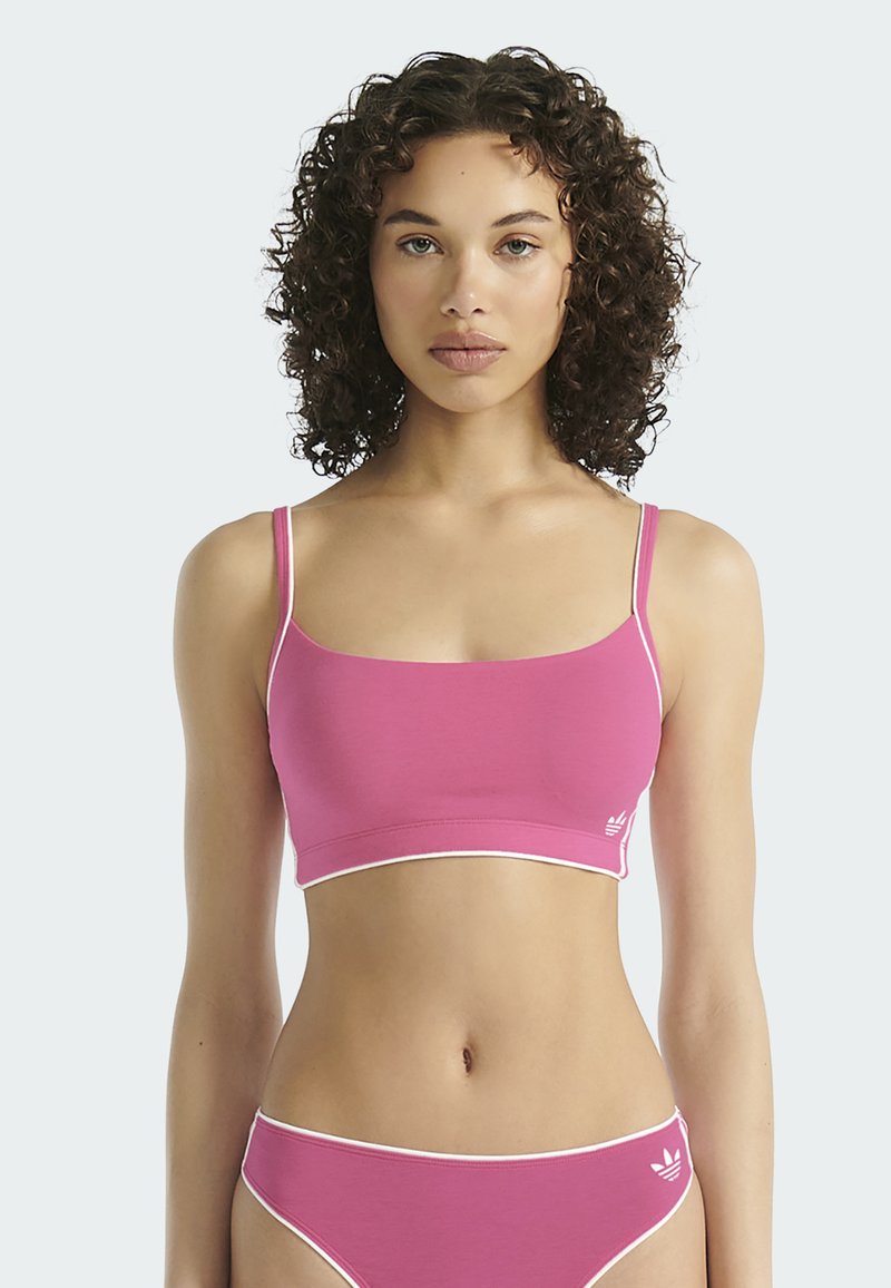 Růžový crop top s tenkými ramínky, který má přiléhavý střih a bílý lem. Spárován s odpovídajícími růžovými kalhotkami s vysokým pasem. Měkká texturka látky.