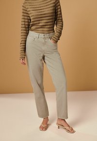 Beige high-waisted jeans met voorzakken, slanke rechte benen, gecombineerd met een bruin gestreepte lange mouwtop en beige hoge hakken sandalen.
