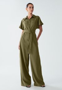 Kaki kombinezon z ovratnikom, kratkimi rokavi, gumbi spredaj, pasom in širokimi hlačnicami; dva sprednja žepa. Gladek tekstura.