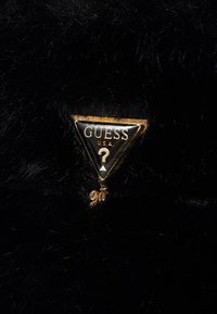 Juodas dirbtinio kailio audinys su auksiniu trikampio logotipu ir tekstu "GUESS U.S.A." bei klausimo ženklo dizainu centre.