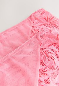 Gros plan d'un tissu de lingerie en dentelle rose avec des motifs floraux et des détails en mesh transparent sur un fond clair.