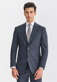 Garnitur w kolorze granatowym o dopasowanym kroju, z dwoma przednimi kieszeniami i zapięciem na guziki. W zestawie jasna koszula i krawat z wzorem.