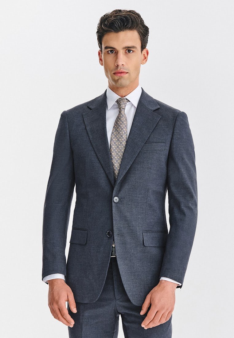 Garnitur w kolorze granatowym o dopasowanym kroju, z dwoma przednimi kieszeniami i zapięciem na guziki. W zestawie jasna koszula i krawat z wzorem.