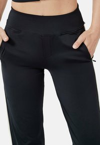 Zwarte sportieve broek gemaakt van glad, rekbaar materiaal met een hoge tailleband en ritszakken aan de zijkant; heeft subtiele witte zijkanten.