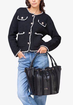 Giacca nera in misto lana con bordi bianchi e chiusura con bottoni, dotata di tasche a toppa. La borsa nera in pelle ha strisce verticali e manici superiori.
