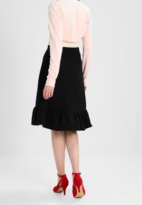 Falda negra con volantes y tejido texturizado, combinada con un suéter corto rosa y zapatos de tacón rojo, vista desde la parte de atrás.