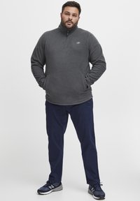 Grau Fleece-Quarter-Zip-Pullover mit Seitentaschen, kombiniert mit navyblauen Hosen und dunklen Sneakers. Bequemes, lässiges Design.