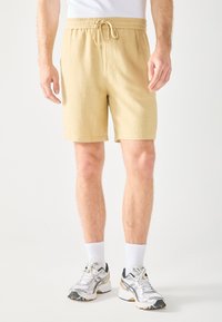 Beige bomulds shorts med elastisk talje og snøre. Har sidelommer, er midt-lår længde og har et tekstureret stof.