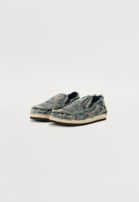 Denim slip-on shoes with frayed edges, a natural jute sole, and a textured blue pattern. Elastic inserts on sides for easy wear.