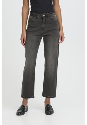 Person iført højtaljede, straight-cut, falmede sorte jeans med knap og lynlås, kombineret med sorte læder loafers og en sort top.