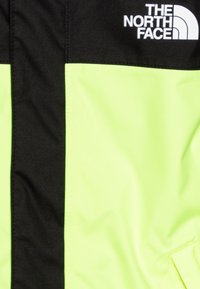 Klart gul och svart jacka med en mjuk textur och logotyp på övre vänstra sidan. Designen inkluderar en vertikal färgseparation och stickningsdetaljer.