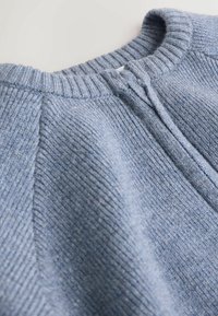 Light blue sweater with ribbed texture, featuring a rounded neckline and a half-zip closure. Soft knit material. Tailored fit design.