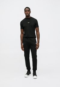 Μαύρο βαμβακερό μπλουζάκι με στρογγυλή λαιμόκοψη, σε συνδυασμό με μαύρο παντελόνι φόρμας και μαύρα παπούτσια. Απλός σχεδιασμός με ελάχιστα λογότυπα.