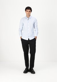 Chemise bleu clair à manches longues, boutonnière, associée à un pantalon noir et des chaussures noires. Design simple avec une coupe ajustée.