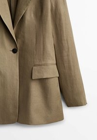 Ruskea pellavablazeri, jossa on yksi musta nappi, lovetalvit ja tasku vasemmassa hihassa, tekstuuripinta.