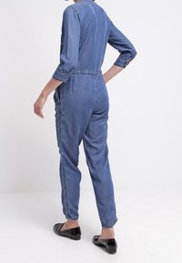 Denimjumpers i ljusblått, med lång ärm, smalnande ben och sidofickor. Texturerad tyg med minimala sömnadsdetaljer.