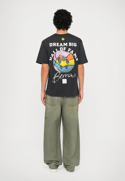 T-shirt in cotone nero con stampa grafica colorata sul retro, con il testo "DREAM BIG" e "HALL OF FAME". Pantaloni in denim verde dalla vestibilità ampia.